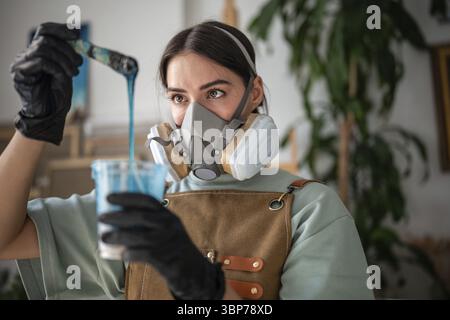 Professionelle Künstlerin rührt Epoxidharz, bewertet Dicke und Konsistenz, um in der Technik der flüssigen Kunst zu arbeiten. Frau, die Flüssigkeit mischt Stockfoto