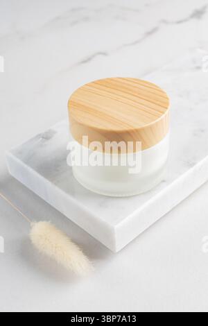 Cremefarbenes Glas auf Marmortablett. Kosmetisches Hautpflegemittel, leere Milchglasverpackung. Weiße Lotion ohne Marke, Balsam, Creme-Mockup. Sonnencreme Flasche wi Stockfoto
