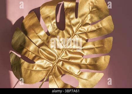 Stilvoller Hintergrund mit Blattgold von Monstera auf rosa Farbe mit Lichtern und Schatten Stockfoto