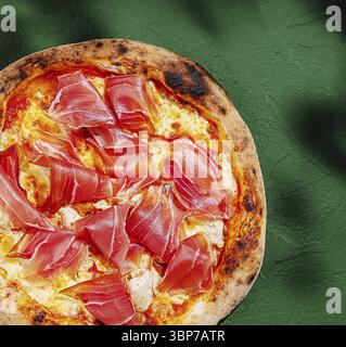 Essen, Eine köstliche Pizza bietet eine knusprige Kruste mit geschmolzenem Käse und großzügigen Scheiben Schinken, die auf einer lebendigen grünen Tischdecke ruhen. Pe Stockfoto