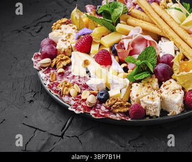 Speisen, verschiedene Käsesorten, Wurstwaren, Nüsse und frisches Obst sind wunderschön auf einer dunklen Platte angeordnet und mit lebhaften Farben und Texturen versehen Stockfoto