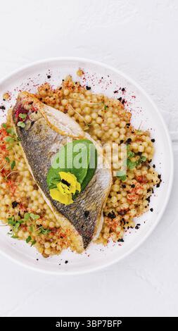 Essen, Blick von oben auf ein gegrilltes Lachsfilet serviert mit gewürztem Couscous, garniert mit Kräutern Stockfoto