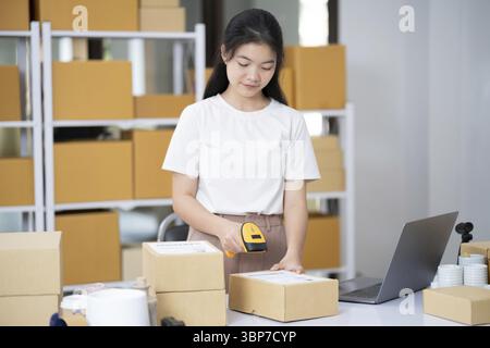 Hände scannen den Barcode auf dem Zustellpaket. Der Mitarbeiter scannt den Barcode von Kartonverpackungen vor der Auslieferung bei der Lagerung. Frau, die im Fabriklager arbeitet, sc Stockfoto
