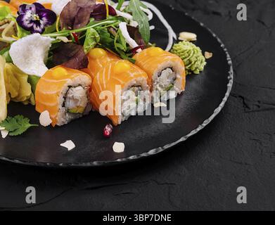 Speisen, Gourmet-Sushi-Brötchen mit lebendigen essbaren Blumen, präsentiert auf einem dunklen Schieferteller Stockfoto