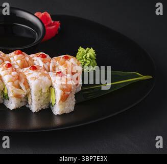 Essen, Sushi-Rolle bedeckt mit Garnelenfleisch auf schwarzer Keramikplatte Nahaufnahme Stockfoto