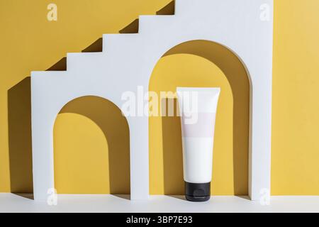 Produktkonzept für Kosmetik. Weiße Tube Creme auf gelbem Hintergrund. Vorderansicht. Trendige Vitrine mit hartem Licht. Paket ohne Branding Stockfoto
