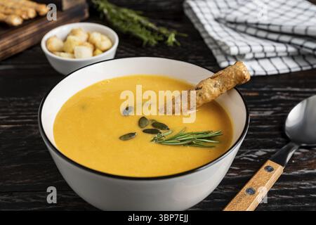 Kürbis- und Karottensuppe mit Sahne, Kürbiskernen, Croutons und Grossini-Brotstangen auf dar k Holzhintergrund. Rustikaler Stil, selektiver Fokus Stockfoto