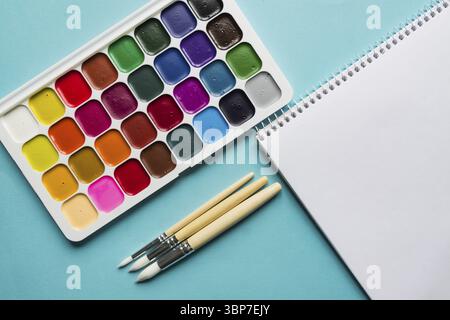 Kreatives Layout mit Aquarellpalette, Pinsel auf blauem Hintergrund. Draufsicht. Künstlerkonzept Stockfoto