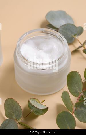 Gesichtscreme auf beigefarbenem Hintergrund. Trockene Eukalyptusblätter Dekoration. Professionelle Flasche für Gesichts- und Körperbehandlungen. Paket ohne Branding Stockfoto