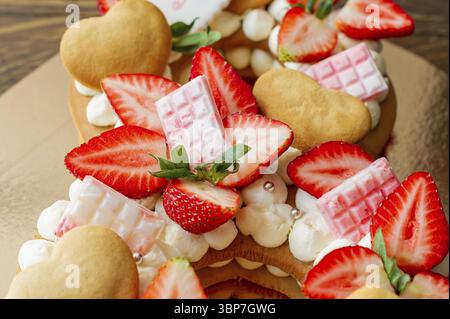 Biskuitkuchen mit Erdbeeren, rosa Milchschokolade, Silberstreuseln, Vanillecreme und herzkranken Keksen aus nächster Nähe. Sommer süßes Dessert für bi Stockfoto