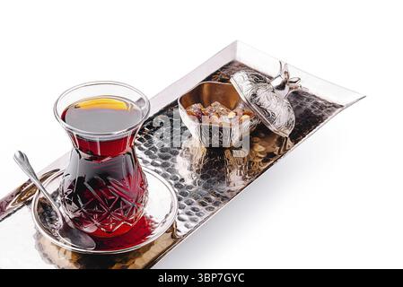 Essen, Eine traditionelle Portion türkischer Tee wird in einem eleganten Glas präsentiert, begleitet von einer dekorativen Schüssel gefüllt mit Zuckerwürfeln auf einem stilvollen Met Stockfoto