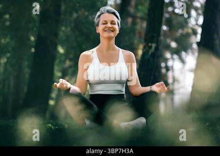 Die lächelnde Frau in Sukhasana posiert mit Freude in der Natur während der Yoga-Praxis im Freien Stockfoto
