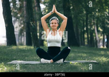 Senior Frau in Sukhasana Yoga posiert Achtsamkeit mit erhobenen Händen im Freien Stockfoto
