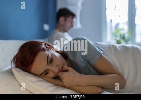 Die verärgerte Frau liegt mit ihrem Rücken zum Ehemann. Frustration, Unglück, Schmerz, Groll und Nachdenklichkeit im Gesicht einer traurigen depressiven Frau, die im Bett lag Stockfoto