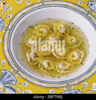 Essen, elegante Keramikplatte mit traditionellen italienischen Tortellini, bestreut mit Kräutern auf strukturiertem Hintergrund Stockfoto