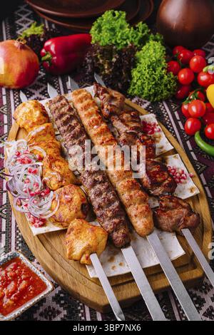 Essen, köstliche traditionelle Grillspießplatte mit gegrilltem Fleisch, verschiedenen Gemüsesorten und scharfer Sauce auf einem Holzbrett für eine Gourmet-Küche Stockfoto