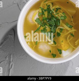 Essen, Blick von oben auf eine gemütliche Schüssel mit Hühnchennudelsuppe garniert mit Petersilie auf einer strukturierten Oberfläche Stockfoto