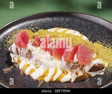 Food, Ein köstliches Dessert, besteht aus cremigen Joghurtschichten mit frischen pinken Grapefruitscheiben und zerstoßenen Pistazien auf einem dunklen Teller. Das Gericht Stockfoto