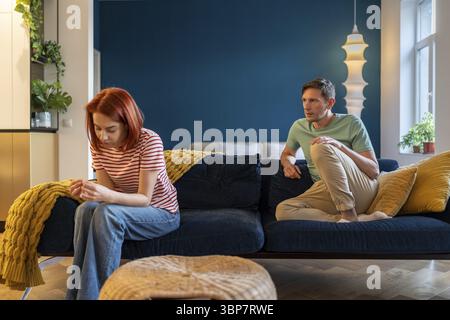 Mann und Frau sitzen getrennt und kommunizieren nicht. Verheiratetes Paar nach lautem emotionalen Streit. Ärgerlich, kalt, ignorierende Ehefrau und ängstlich besorgter Husba Stockfoto