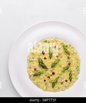 Essen, köstliches Risotto mit Spargel und knusprigen Pancetta-Stücken, serviert auf einem weißen Teller Stockfoto