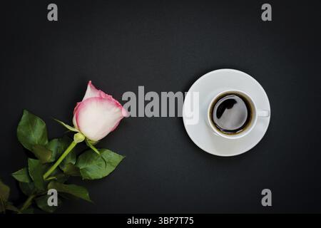 Tasse schwarzen Kaffee und rosa Rose auf schwarzem Hintergrund, Draufsicht, Kopierraum Stockfoto