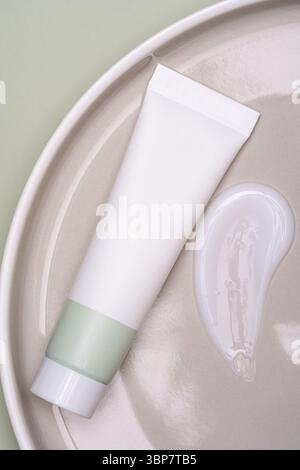 Drücken Sie die Kunststoffröhre und den Cremestrich auf die Keramikplatte. Unverkennbares Paket für Gesichtscreme oder Maske. Hautpflege-Schönheitsbehandlungspräsentation. Mocku Stockfoto