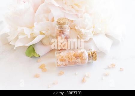 Beauty- und Spa-Konzept. Rosafarbenes himalaya-Salz in Glasboteln, ätherisches Öl und Pfingstrosenblüte im Hintergrund. Selektiver Fokus Stockfoto