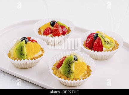 Essen, elegante Tartlets mit Kiwi-, Orangen- und Erdbeerscheiben auf Keramikplatte Stockfoto