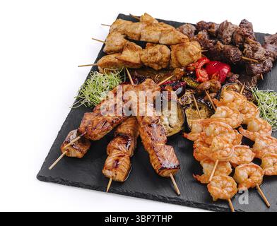 Speisen, Eine Vielzahl gegrillter Spieße auf einer Schieferplatte mit Garnelen, Huhn, Rindfleisch und verschiedenen Gemüsesorten. Die farbenfrohe Präsentation Stockfoto