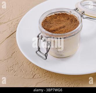 Essen, Tiramisu, traditionelles italienisches Dessert in einem Glas, präsentiert auf einem weißen Gericht mit strukturiertem Hintergrund Stockfoto