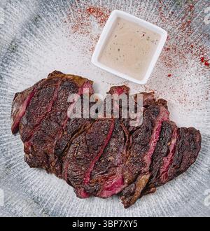 Essen, in Scheiben geschnittenes gegrilltes Rindersteak, das auf einem Teller mit Sauce liegt und mit Gewürzen abgeschmeckt wird Stockfoto