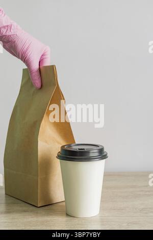 Weibliche Hand in schützenden rosa medizinischen Handschuhen liefert Essen zum Mitnehmen. Das Lieferdienstkonzept während der Coronavirus-Pandemie Stockfoto