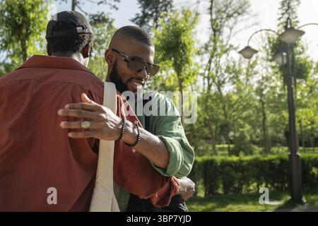 Zufriedene, fröhliche Schwarze, die sich auf der Straße umarmen. Plötzliches, unerwartetes freudiges Treffen von Männern, männlichen Studenten, Freunden im Park draußen. Klassenkameraden br Stockfoto