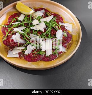 Essen, köstliche Vorspeise aus dünn geschnittenem rohem Rindfleisch mit Parmesankäse, Kapern und Rucola auf Teller Stockfoto