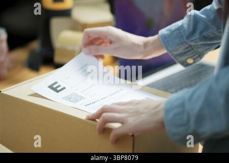 Versandetikett an einem Paket anbringen. Versandvorbereitung für E-Commerce-Unternehmen. Nahaufnahme der Etikettierung von Verpackungen Stockfoto