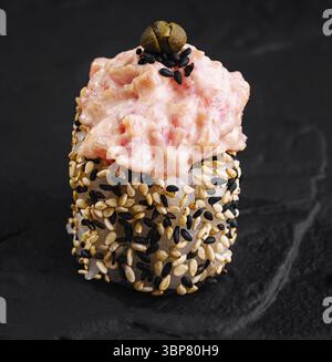 Speisen, kunstvoll präsentierte scharfe Thunfisch-Sushi-Rolle, garniert mit Sesamsamen auf einem dunklen Schieferhintergrund Stockfoto