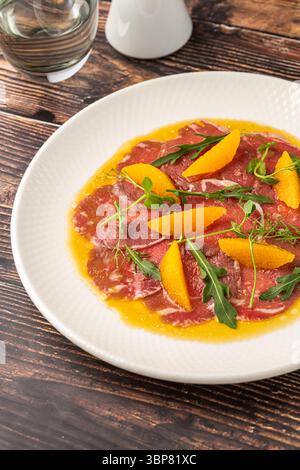 Dünn geschnittenes Rindfleisch-Carpaccio mit Orangensegmenten und Rucolablättern Stockfoto