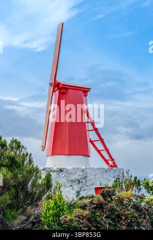 Lebendige traditionelle Rote Windmühle auf einem grasbewachsenen Hügel in Urzelina, Sao Jorge Island, Azoren, unter einem dynamischen blauen Himmel. Azoren Erbe, Histo Stockfoto