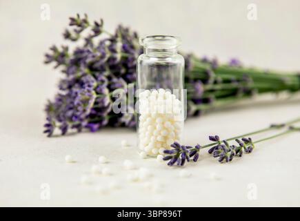 Lavendelblüten mit weißen runden Homöopathiepillen in der medizinischen Flasche. Homöopathie-Konzept. Stockfoto