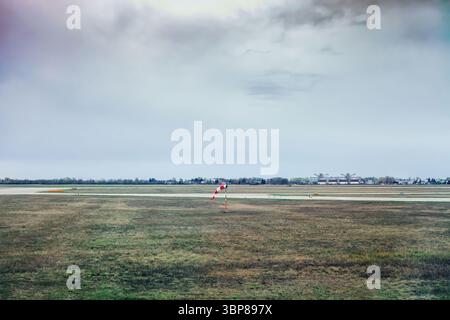 Windsocke auf dem Flugplatz. Rot-weiß fliegende Anemometer zur Anzeige der Windrichtung und -Geschwindigkeit auf der Grasebene in der Nähe der Start- und Landebahn. Windsockungsanzeige am Flughafen Stockfoto