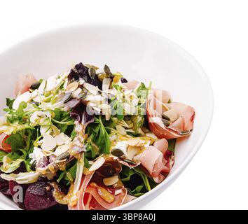 Essen, Ein lebendiger Salat mit einer Mischung aus Gemüse, Schinkenscheiben, Mandeln und Kürbiskernen. Dieses farbenfrohe Gericht wird in einer weißen Schüssel serviert Stockfoto
