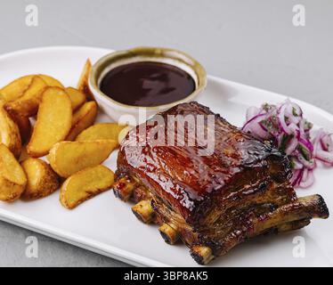 Essen, köstliche Platte mit glasierten Schweinerippchen mit Kartoffelscheiben, bbq-Sauce und Slaw auf einem weißen Teller Stockfoto