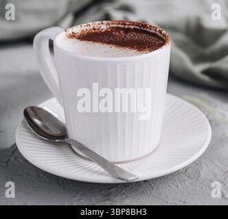 Essen, gemütliche Szene mit einer weißen Tasse Cappuccino mit Schaumkunst, einem Löffel und Grün Stockfoto