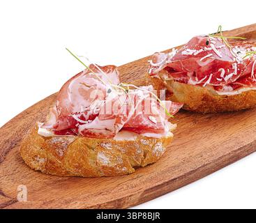 Essen, zwei Scheiben knuspriges Brot mit dünn geschnittenem Wurstfleisch werden auf einem Holzbrett präsentiert. Dieses schmackhafte Gericht präsentiert feine kulinarische cr Stockfoto