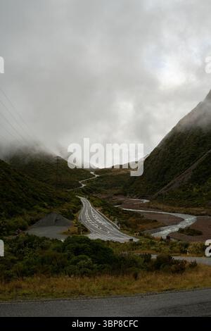 Moody, ruhige Talszene. Eine gewundene Straße schlängelt sich durch einen dichten, smaragdgrünen Wald, der in Nebel gehüllt ist. Ein Gefühl von Isolation und zeitloser Schönheit, evoki Stockfoto