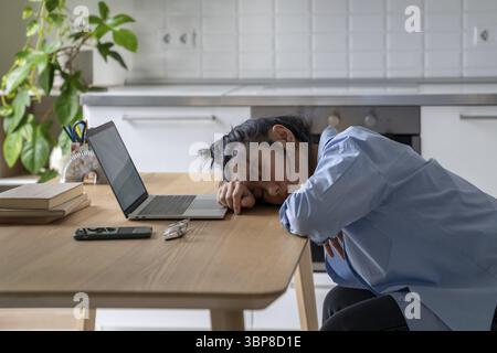 Erschöpfte asiatische Frau sitzt überarbeitet braucht Ruhe Ermüdung beim Nickerchen in der Nähe des Laptops. Müde Chinesin Studentin oder Freiberuflerin schlief auf dem Tisch ein, während ich Stockfoto