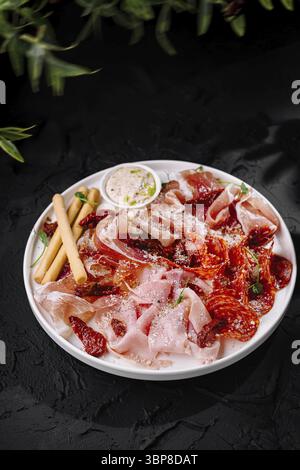 Essen, Gourmet-Auswahl an Räucherfleisch, serviert mit Brotstangen und Sauce vor dunkler Kulisse Stockfoto