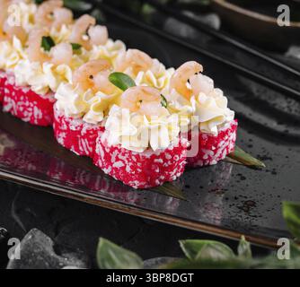 Essen, exquisite Sushi-Brötchen mit Garnelen, Kaviar und cremiger Sauce auf einem eleganten schwarzen Teller Stockfoto