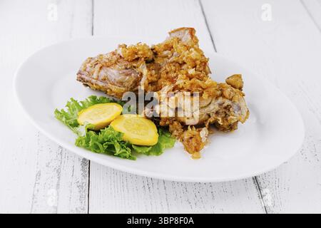 Essen: Zwei Portionen gebratene Hähnchenschenkel werden auf einem weißen Teller serviert, garniert mit Salat und Zucchini-Scheiben Stockfoto