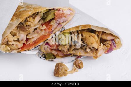 Essen, zwei Hälften appetitlicher Shawarma gefüllt mit Huhn, Gemüse und Sauce liegen auf weißem Hintergrund Stockfoto